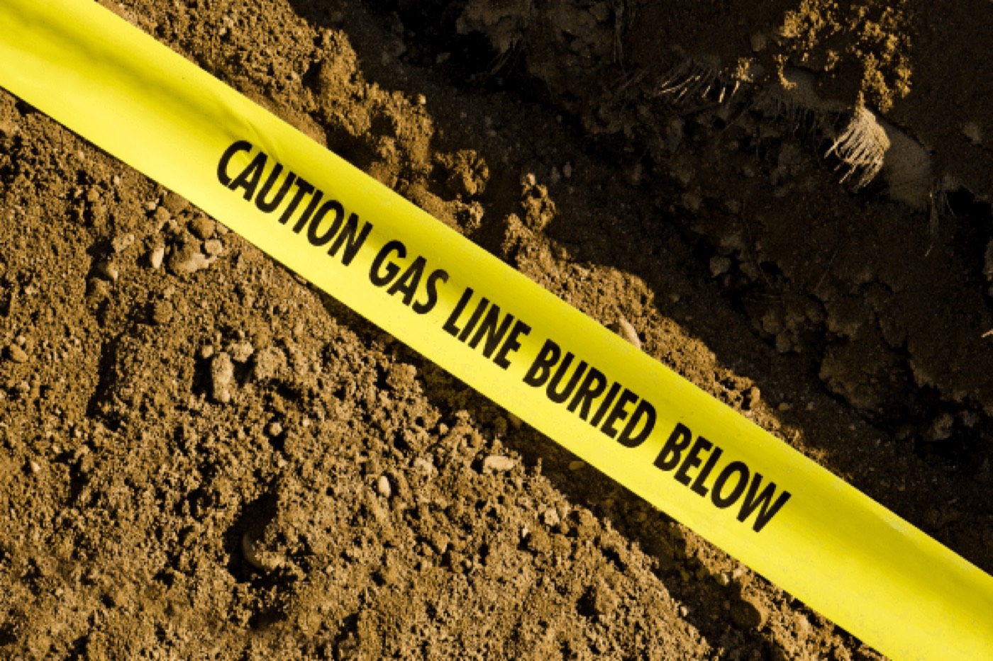 Buried gas line warning tape uncovered while excavating beside a foundation