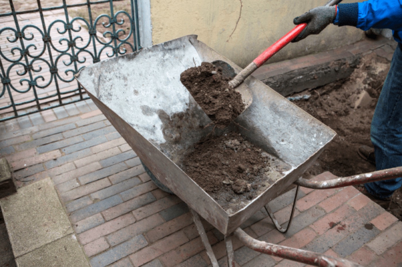 Soil being dug out of a window well beside an existing basement window