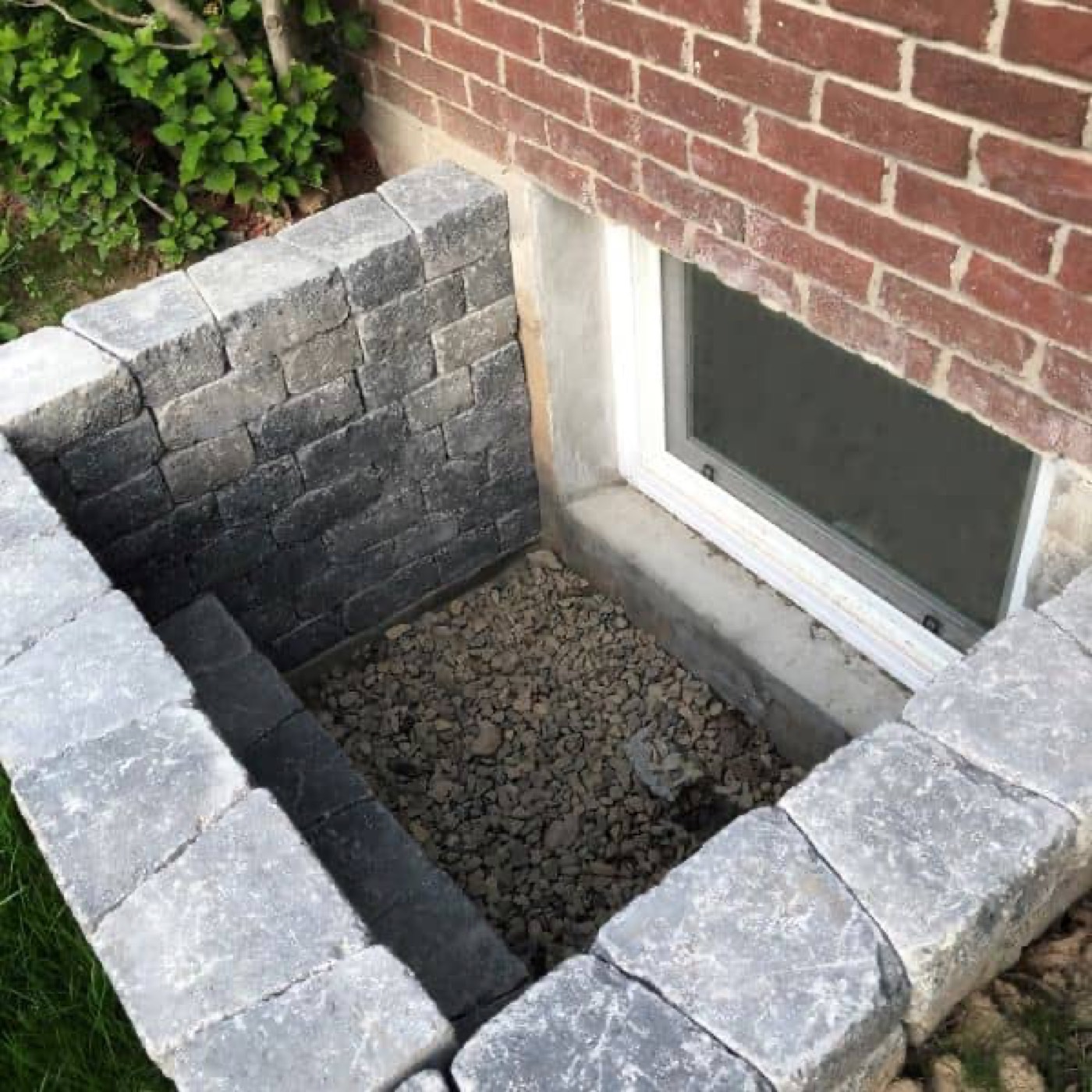 A block and stone wall built up around a window well, still under construction