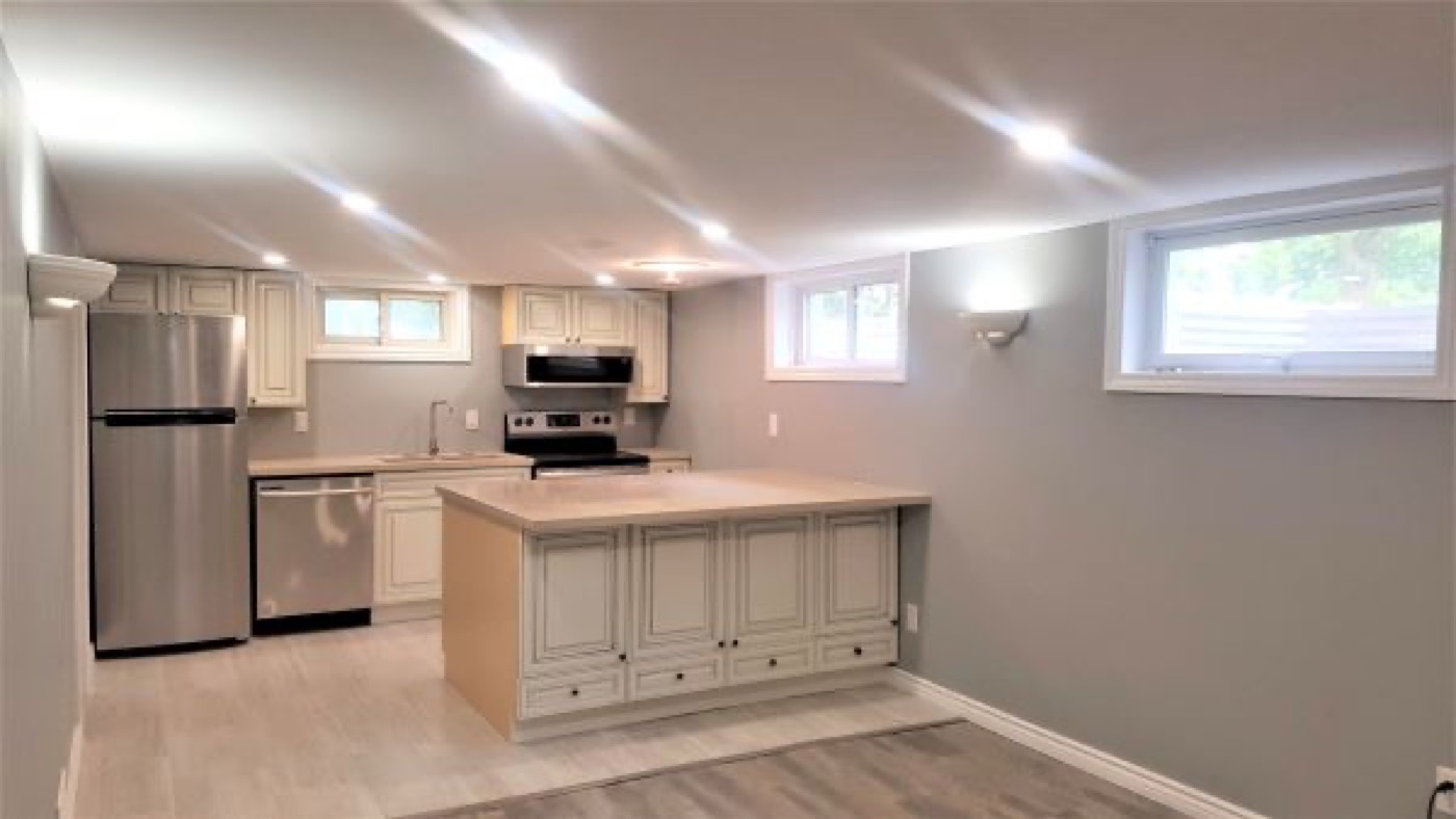 A basement kitchen with two windows set high in the wall above the counter