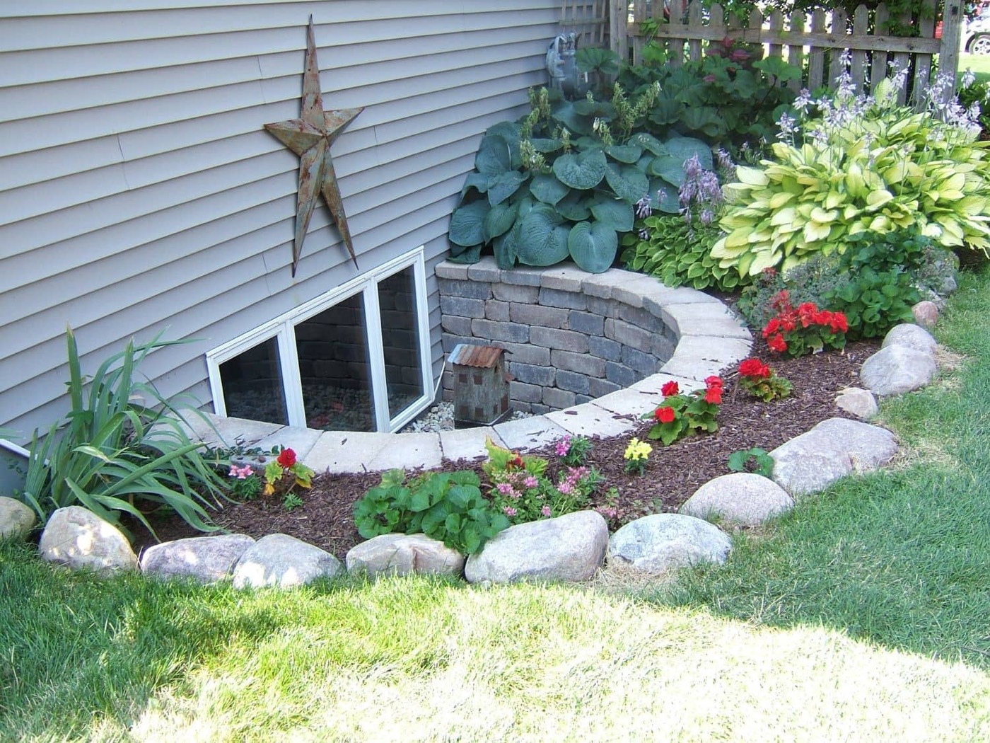 A window well edged with brick pavers and planted borders